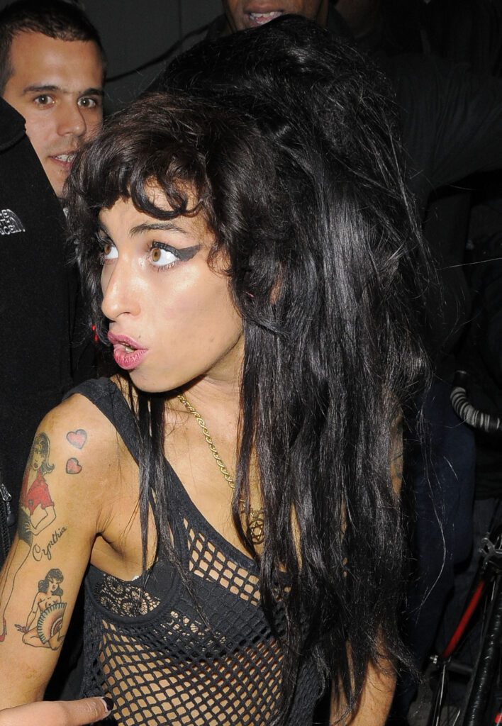 Amy Winehouse runs through Camden with her god daughter Dionne Bromfield, and some security guards. Amy was in a bad mood, having been told at a petrol station they had no playing cards to sell her, and threw a pint glass at a photographer, slapped a passerby in the face and shouted and swore at people in the street. Amy wore a black mesh vest, black bra, denim shorts and her trademark ballet pumps. She appeared to have a lot of fake tan on her hands. Winehouse was plagued by drug and alcohol addiction throughout her life. She died of alcohol poisoning on 23 July 2011 at the age of 27. After her death, Back to Black became the UK's best-selling album of the 21st century temporarily. 15 Aug 2008 Pictured: Amy Winehouse. Photo credit: Will / MEGA TheMegaAgency.com +1 888 505 6342 (Mega Agency TagID: MEGA652375_024.jpg) [Photo via Mega Agency]