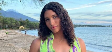Maya Brady stands in front of the camera while at the beach, wearing a matching crop top and skirt.
