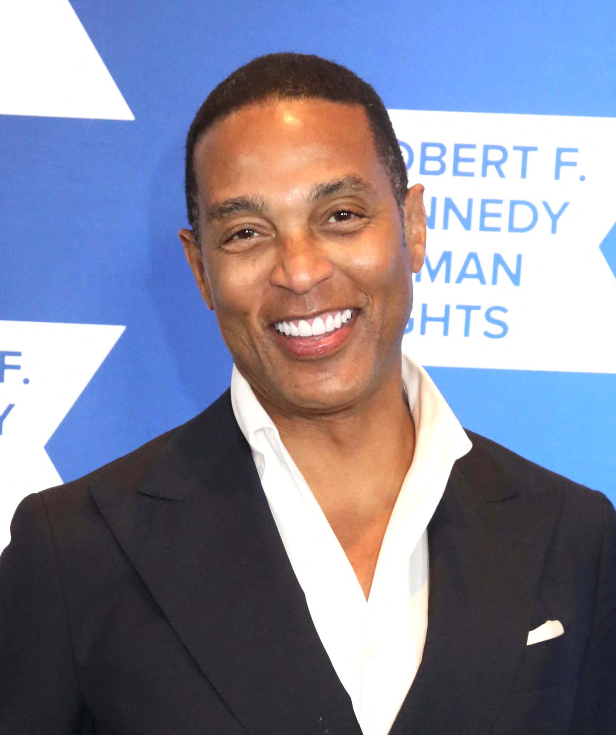 Don Lemon posing in a black suit and smiling.