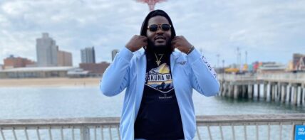 Ronald Ollie in a blue tracksuit in front of a beach.