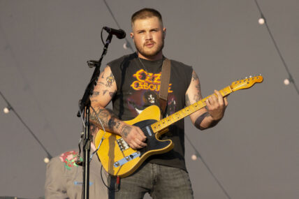 Zach Bryan playing guitar during a show.