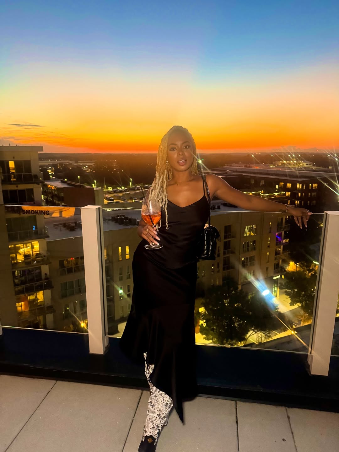 Mickey Lee posing in front of a sunset on a rooftop bar