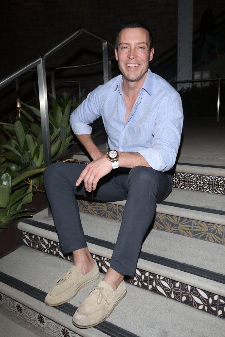 Man in jeans and blue shirt sitting on steps.