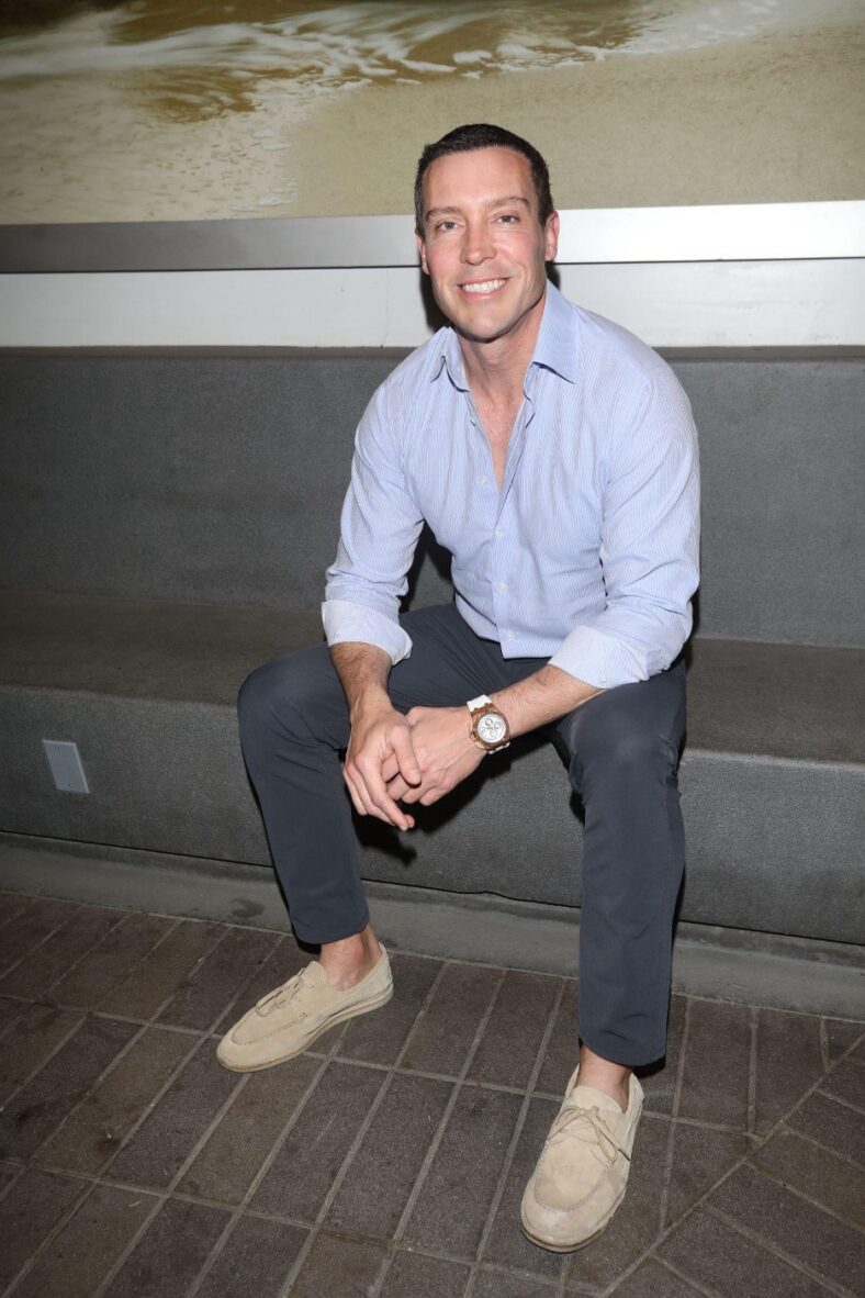 Man in jeans and blue shirt sitting on bench.