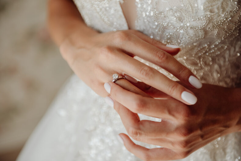 Hands of the bride in a white wedding dress with a gold engagement ring with a diamond close-up