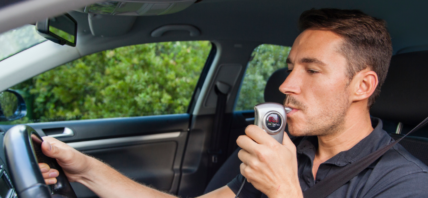 Man in car using breathalyzer.