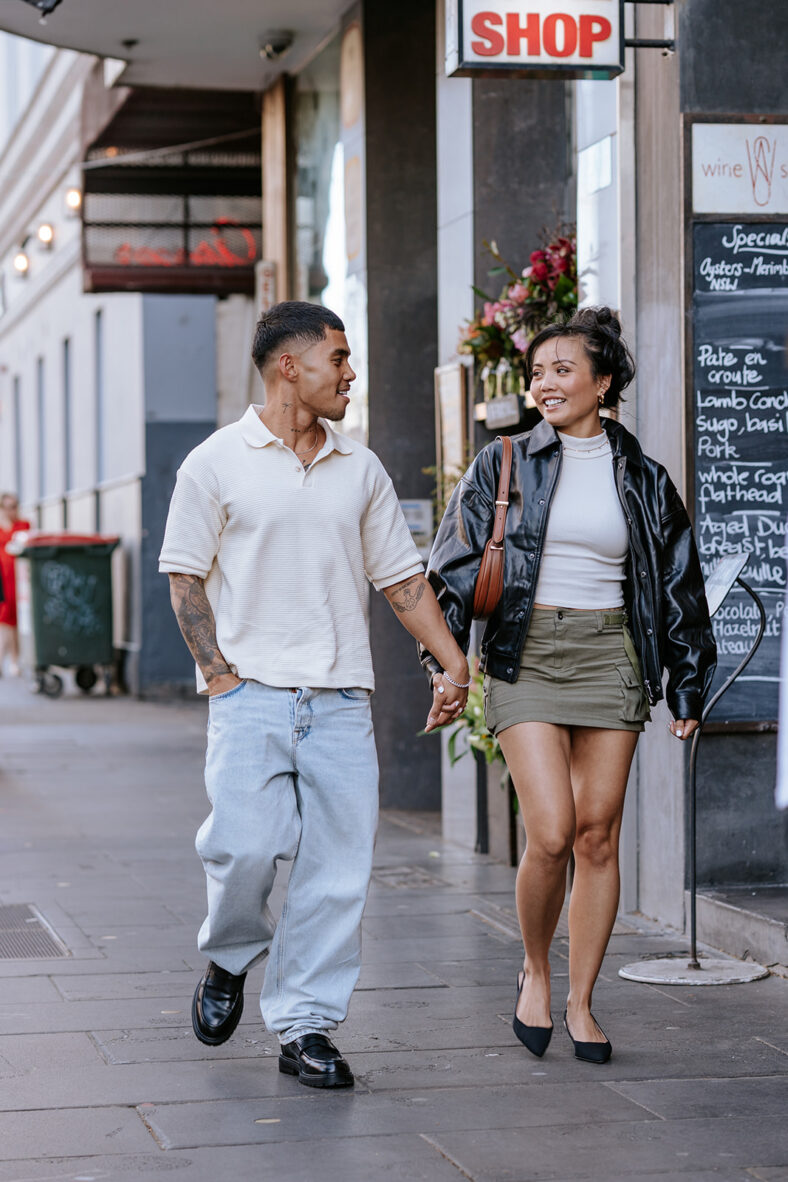 Man and woman holding hands, walking down the street.