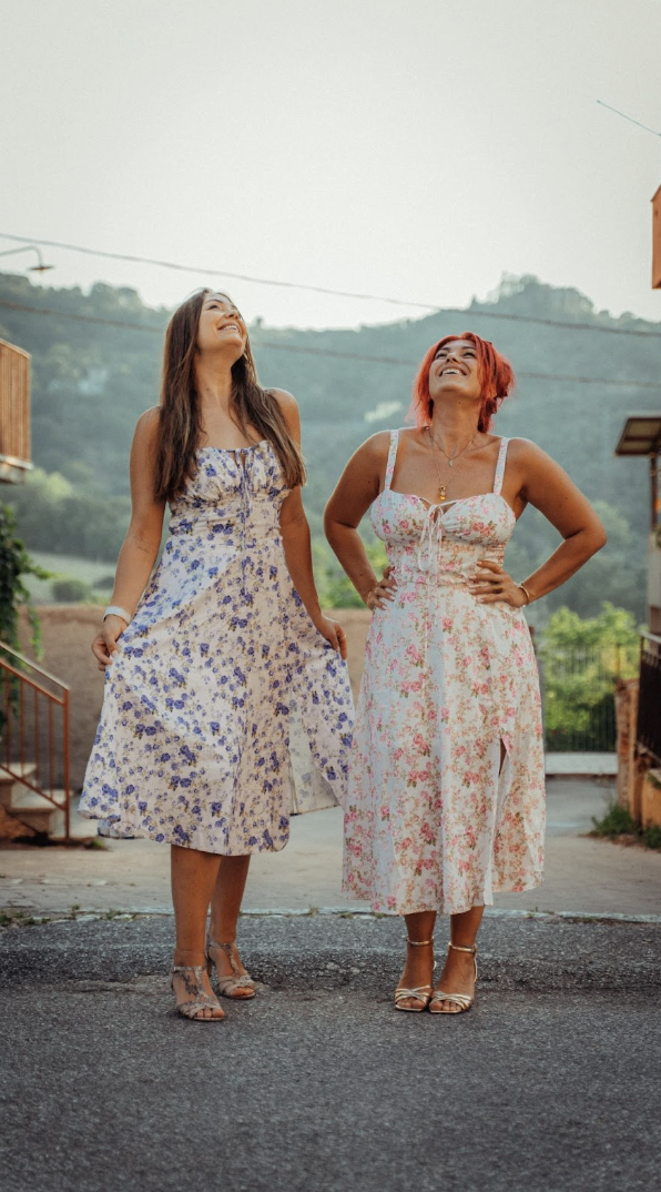 Two woman in floral dresses smiling at the sky.